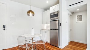A modern kitchen with white cabinets, a stainless steel refrigerator, a microwave, and a round table with clear chairs.