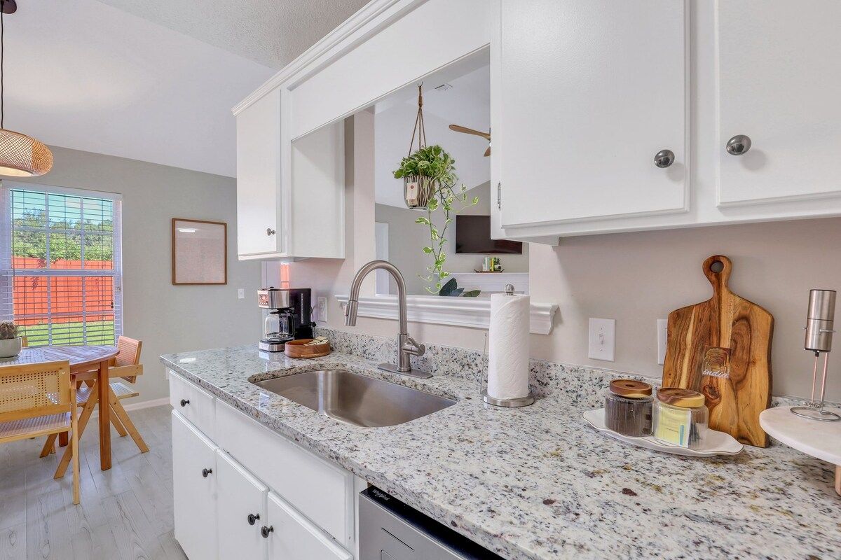 A kitchen with a granite countertop, stainless steel sink, and white cabinetry.