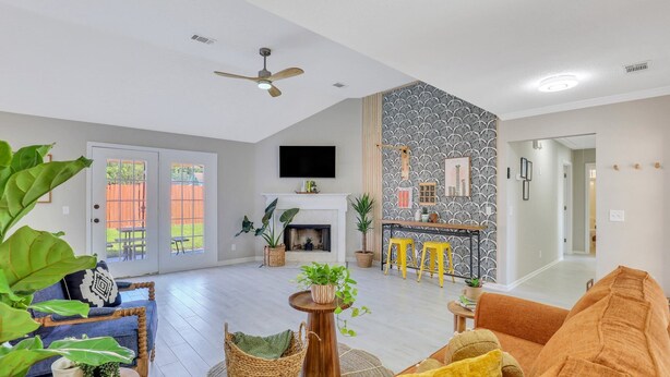A spacious living area with a fireplace, a ceiling fan, and a kitchen area with a patterned backsplash. - Stay Near Gulfstream, Outlets & Airport (Pooler)