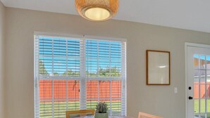 A dining area with a round wooden table, four chairs, a hanging light fixture, and a window with blinds. - Stay Near Gulfstream, Outlets & Airport (Pooler)