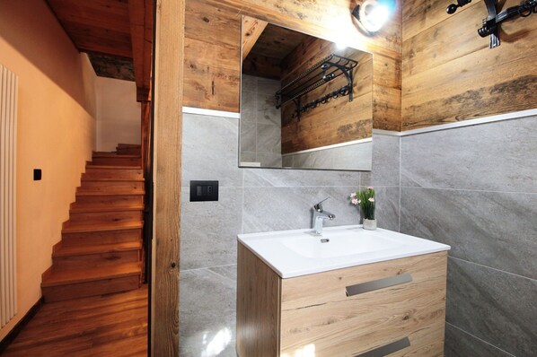 Un baño con tocador de madera, lavamanos y espejo.