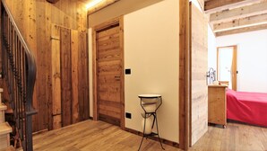 Ein Zimmer mit Holzboden, einer Treppe, einer Tür, einem kleinen Tisch und einem Bett mit roter Bettdecke.