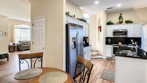 A modern kitchen with white cabinets, stainless steel appliances, and a dining area with a wooden table and chairs. - Triton Vacation Pool Home Near Disney (Clermont)