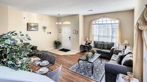 A spacious living room with a dining area, a sofa set, and a large window with blinds. - Triton Vacation Pool Home Near Disney (Clermont)