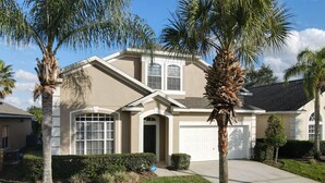 A residential house with a beige exterior, a garage, and a well-maintained lawn with palm trees. - Triton Vacation Pool Home Near Disney (Clermont)