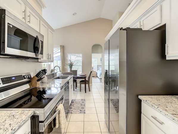A modern kitchen with stainless steel appliances, a marble countertop, and a view to the dining area. - Glenbrook Vacation Pool Spa Home (Clermont)