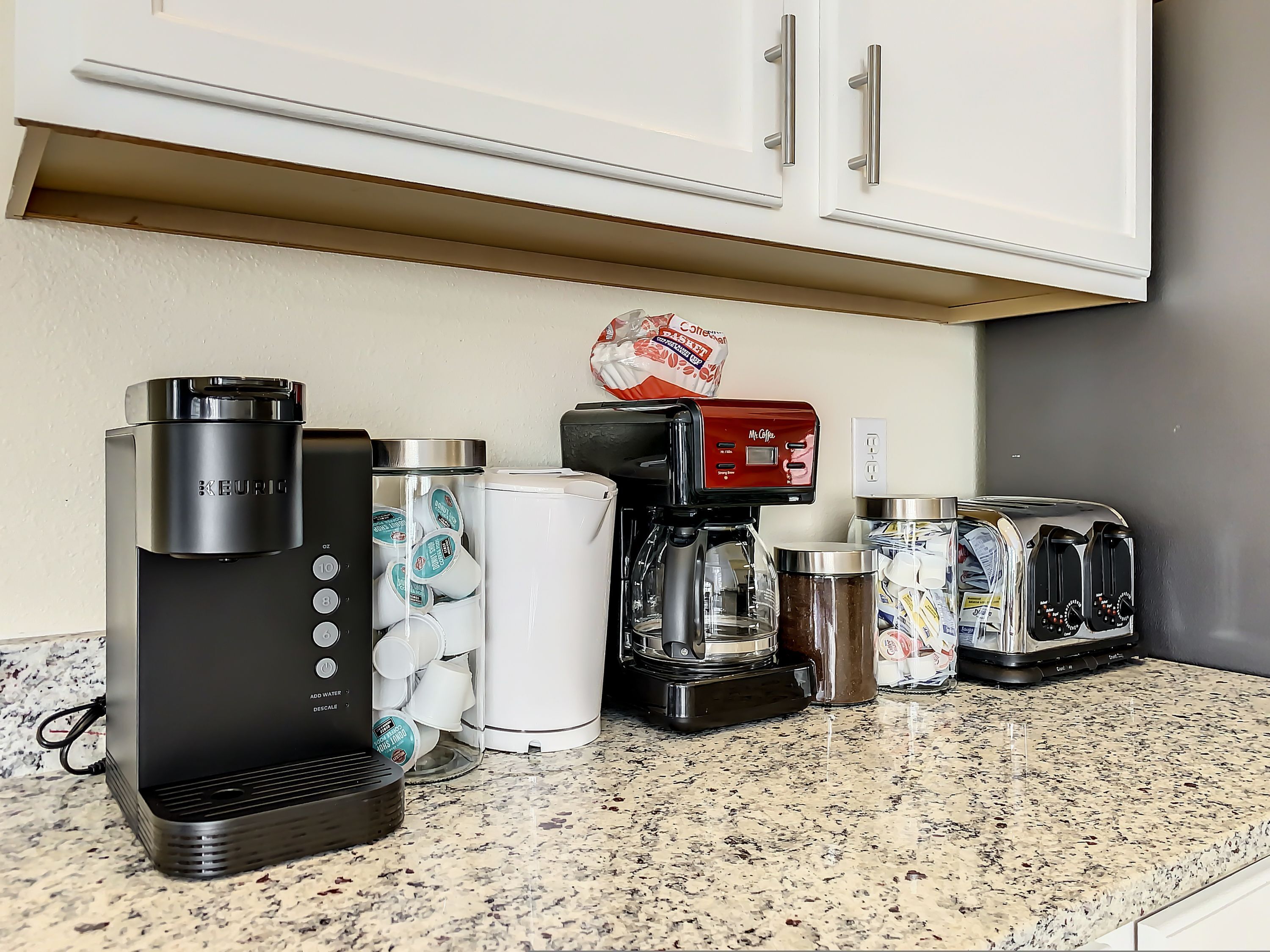 A kitchen counter with various appliances including a Keurig coffee maker, a Mr. Coffee coffee maker, a coffee grinder, and a toaster.