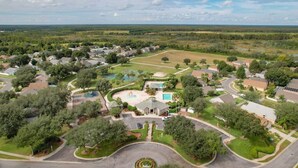 An aerial view of a residential area with houses, a central building with a pool, and surrounding greenery. - Flounder Vacation Home (Clermont)