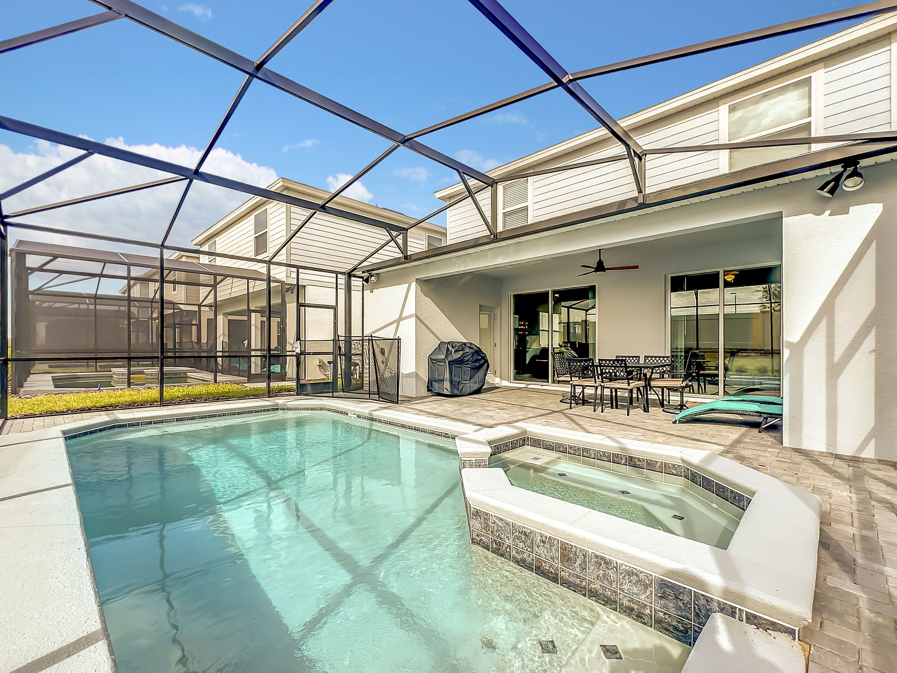 A swimming pool with a glass enclosure, a patio area with outdoor furniture, and a covered patio with a ceiling fan.