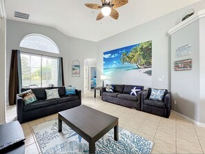 A spacious living room with two dark sofas, a coffee table, and a large beach-themed wall mural. - Beach Theme Vacation Pool Spa Home Mins to Disney (Clermont)