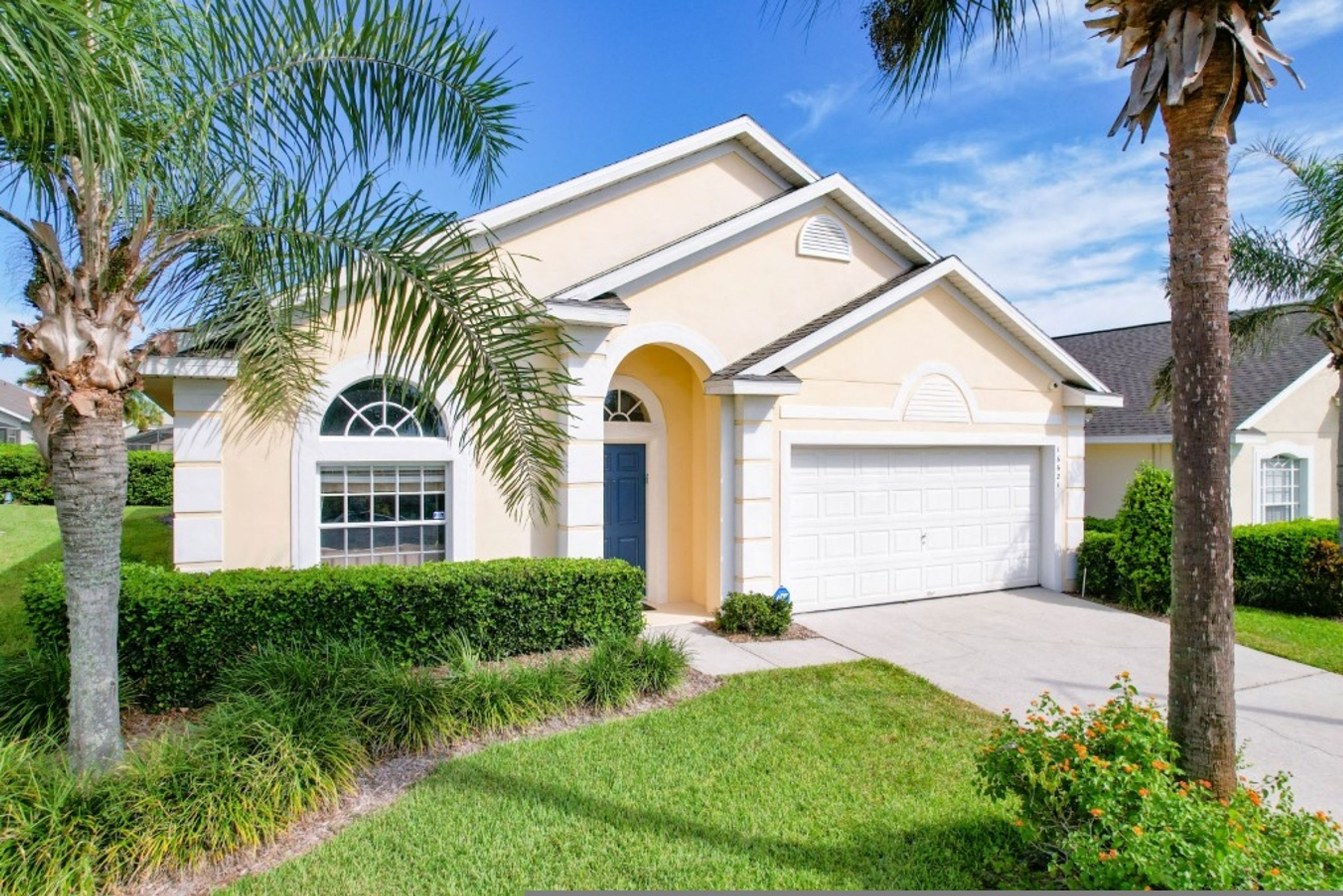 A single-story house with a garage, surrounded by well-maintained landscaping including palm trees and hedges.