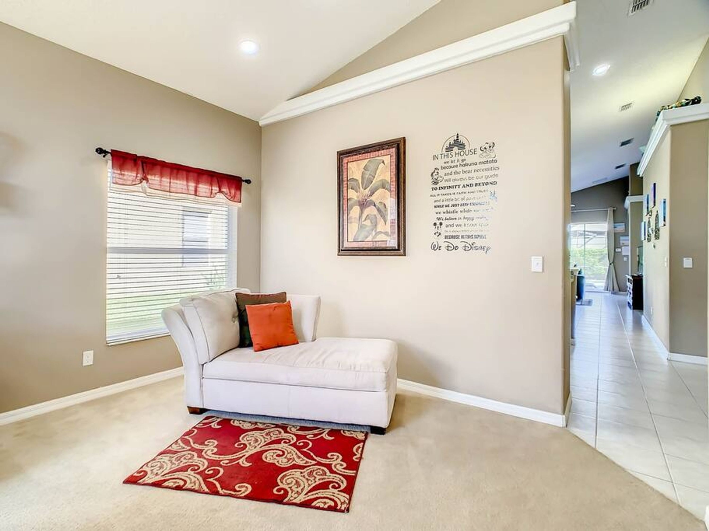 A living room with a white sofa, red and white patterned rug, and a window with blinds.