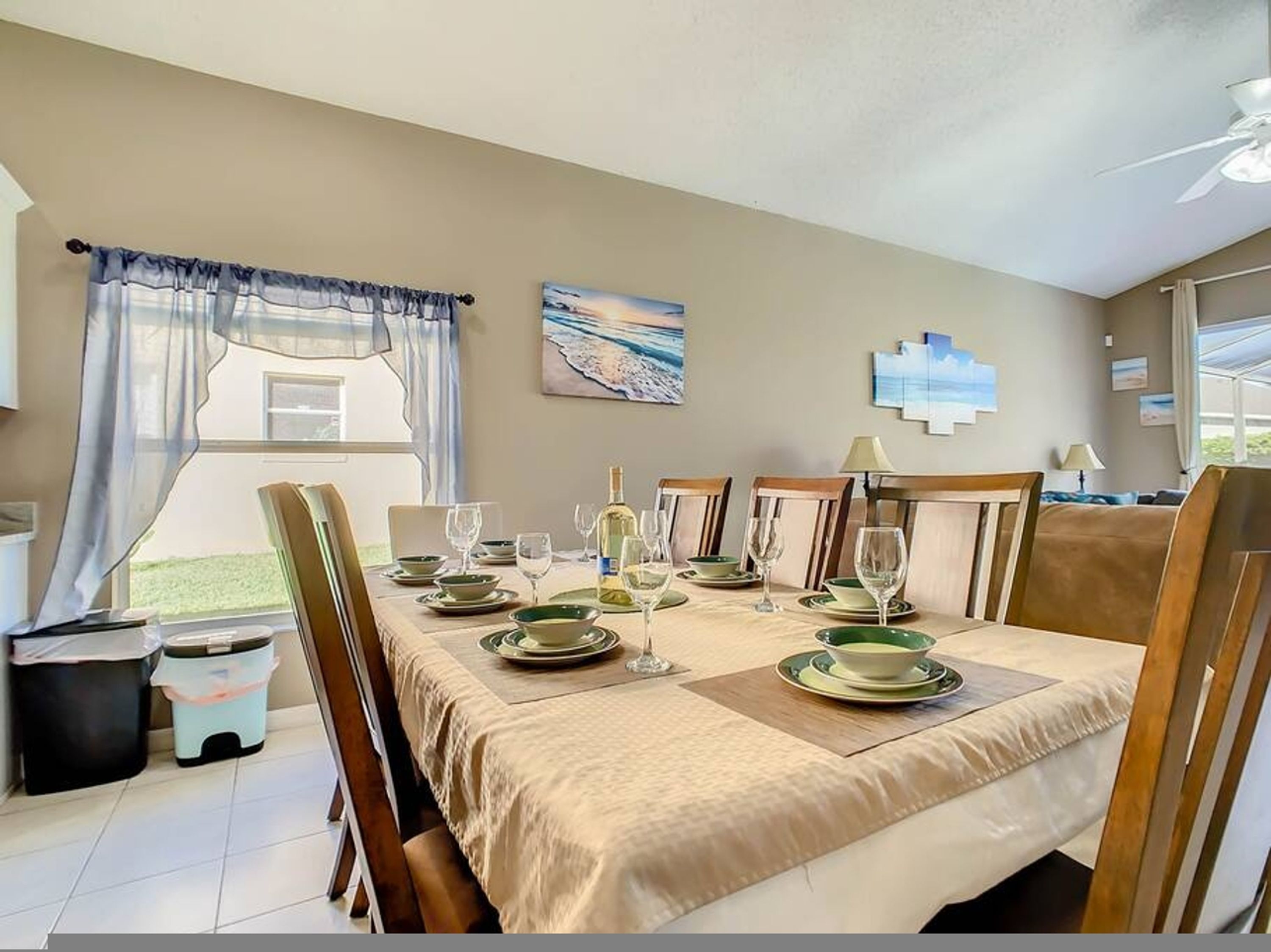 Un coin repas avec une table dressée pour quatre personnes, des chaises, un tableau au mur et une fenêtre avec des rideaux.