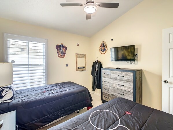 Un dormitorio con dos camas, ventilador de techo, televisor y armario.