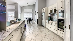 Een moderne keuken met witte kasten, een granieten aanrechtblad, roestvrijstalen apparatuur en een eethoek met een tafel en stoelen.