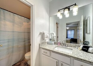A bathroom with a shower curtain, toilet, sink, and mirror. - Scuttle Vacation Pool Home W Spa (Clermont)