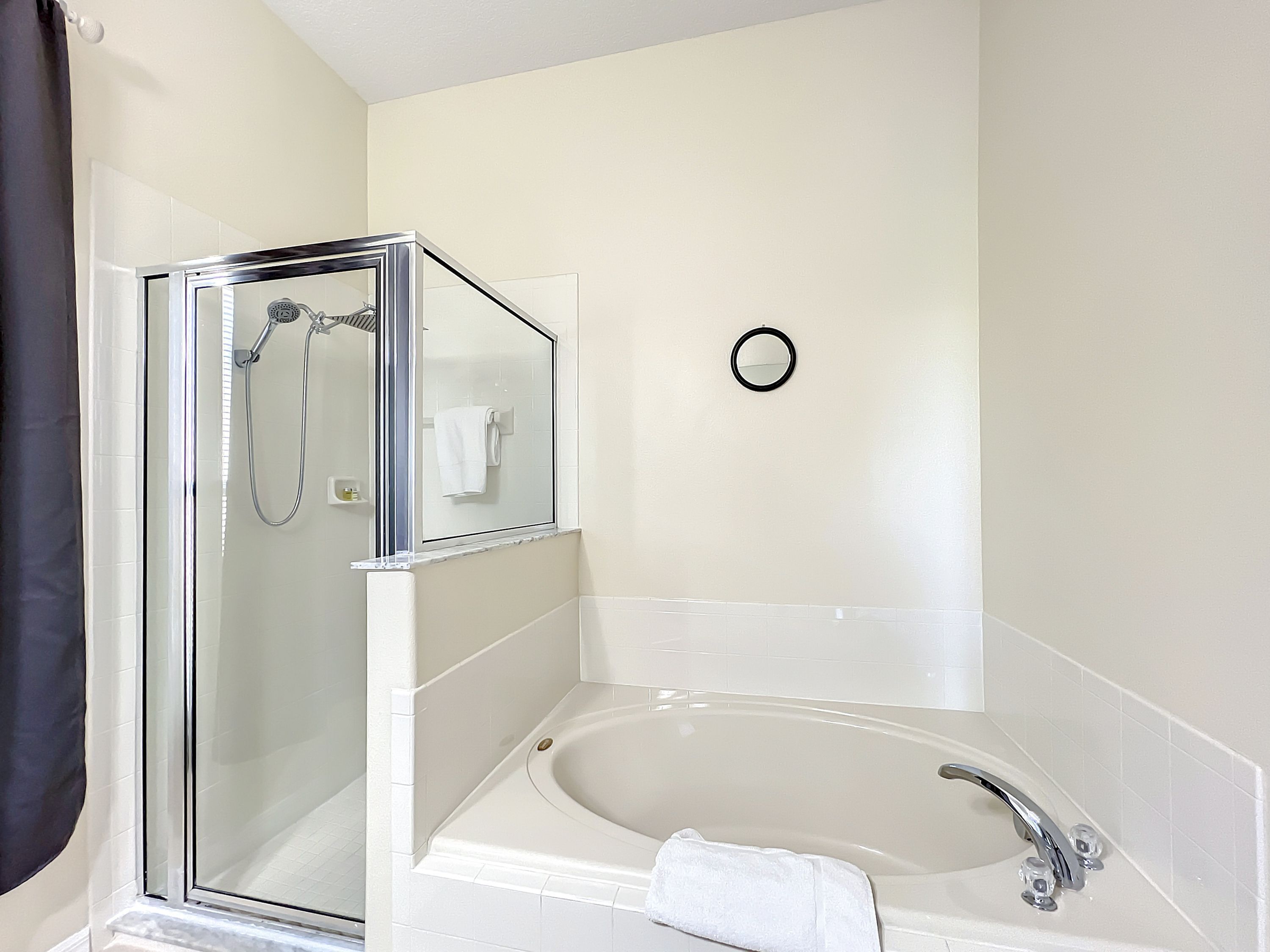 Une salle de bain moderne avec une douche à parois de verre, une baignoire sur pieds et un miroir rond fixé au mur.