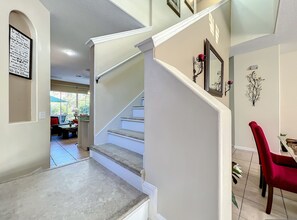 A staircase with a handrail, a dining area with a red chair, and a wall with a framed sign. - Scuttle Vacation Pool Home W Spa (Clermont)