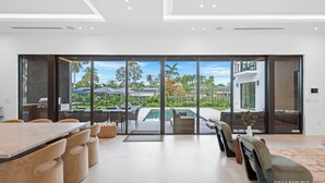 Ein moderner Essbereich mit großem Tisch und Stühlen, Blick auf einen Pool sowie eine geräumige Terrasse mit Sitzgelegenheit im Freien.