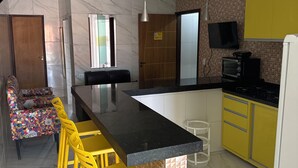 Een moderne keuken met een marmeren spatwand, gele barkrukken, een inbouwoven en een flatscreen televisie.