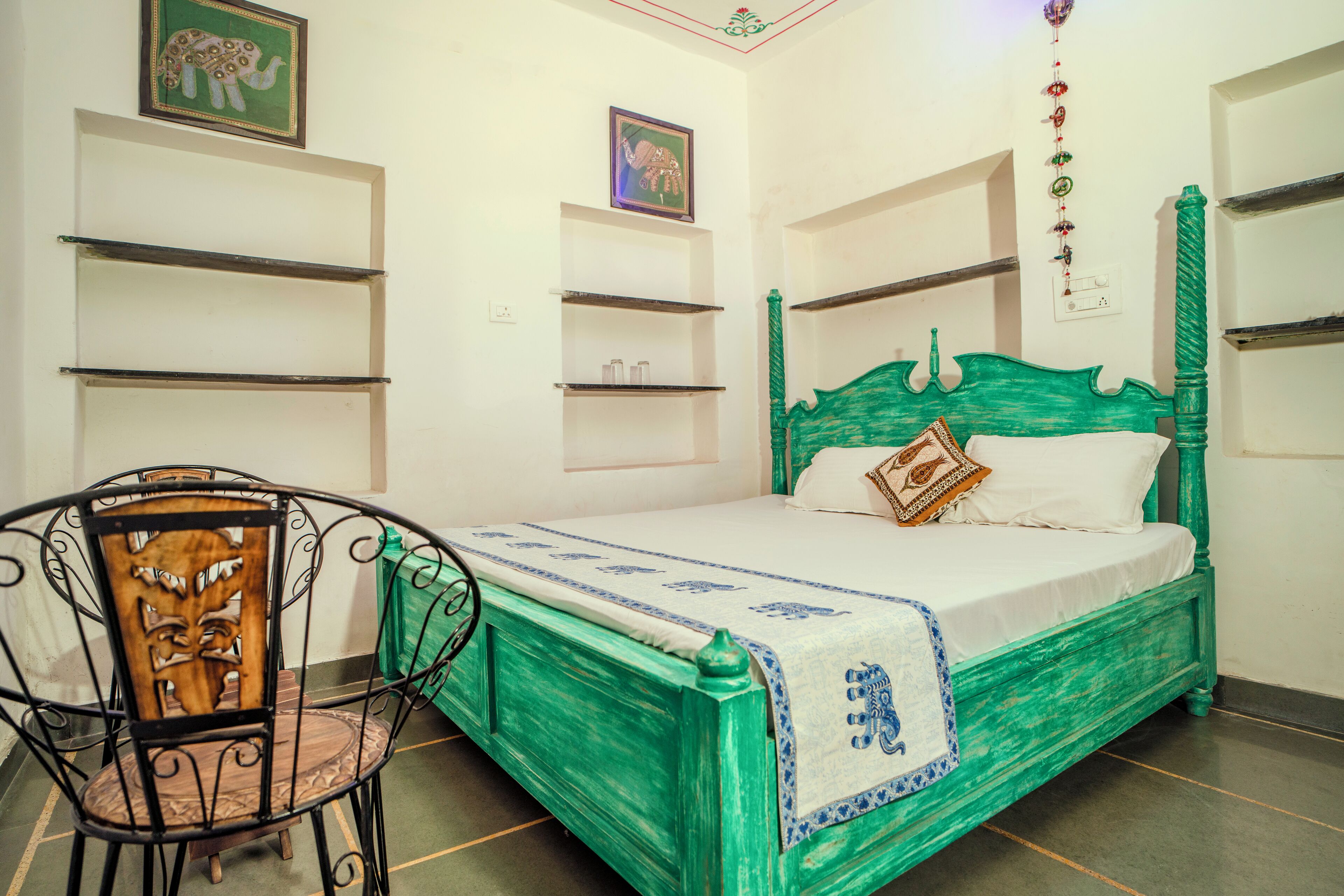A room with a green bed, a chair with a carved backrest, and shelves on the walls.