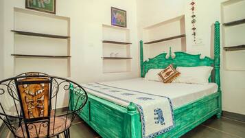 Ein Zimmer mit einem grünen Bett, einem Stuhl mit geschnitzter Rückenlehne und Regalen an den Wänden.