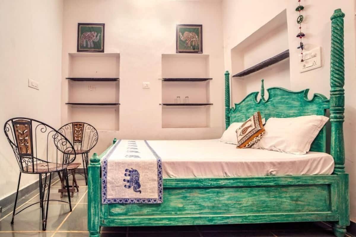 A room with a green bed, two chairs, and wall-mounted shelves.