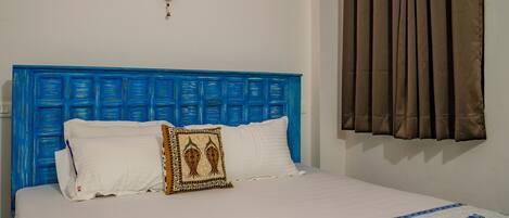 Una cama con cabecera azul, ropa de cama blanca y un cojín decorativo.