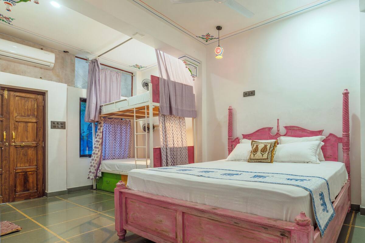 A bedroom with a pink bed, a bunk bed, and a wooden door.
