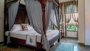 A four-poster bed with a canopy, a patterned bedspread, and a blue and white patterned curtain. - Soham Haveli Udaipur (Udaipur)