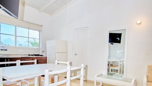 Um quarto claro e arejado, com uma janela grande, TV de tela plana, geladeira e um banco.