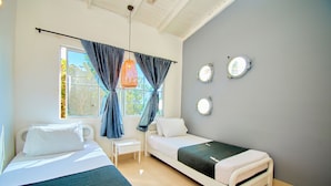 Quarto com duas camas, uma mesa pequena e janela com cortinas.