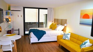 A bedroom with a bed, a yellow sofa, a white table with chairs, and a balcony with a view. - Steps from Waikiki Beach  Pool + Jacuzzi (Honolulu)