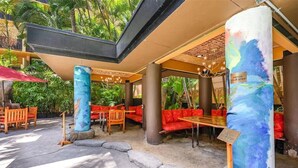 An outdoor seating area with red cushioned benches and tables, surrounded by tropical plants and a stone pathway. - Steps from Waikiki Beach  Pool + Jacuzzi (Honolulu)