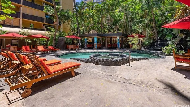 A hotel pool area with lounge chairs, umbrellas, and a water feature. - Steps from Waikiki Beach  Pool + Jacuzzi (Honolulu)