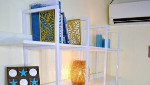 A white shelving unit with decorative items, a wall-mounted air conditioner, and a wooden floor. - Steps from Waikiki Beach  Pool + Jacuzzi (Honolulu)