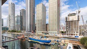 A waterfront cityscape with high-rise buildings, a dock with boats, and a construction crane. - Bright and Stylish Riverside Haven in Canary Wharf (London)