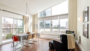 A modern living room with a dining area, large windows with city views, and a black armchair. - Bright and Stylish Riverside Haven in Canary Wharf (London)