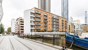 A modern apartment building with balconies, a canal, and a boat docked nearby. - Bright and Stylish Riverside Haven in Canary Wharf (London)