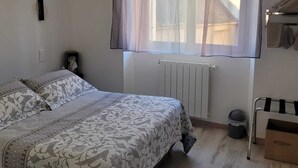 A bedroom with a bed, a radiator, a window with sheer curtains, and a radiator cover. - l Aurigast (Auriac-Lagast)