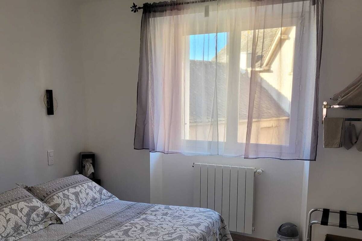A bedroom with a bed, a radiator, a window with sheer curtains, and a radiator cover.