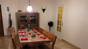 A dining area with a wooden table set for four, a cabinet with glass doors, a fan, and a door with yellow panels. - l Aurigast (Auriac-Lagast)