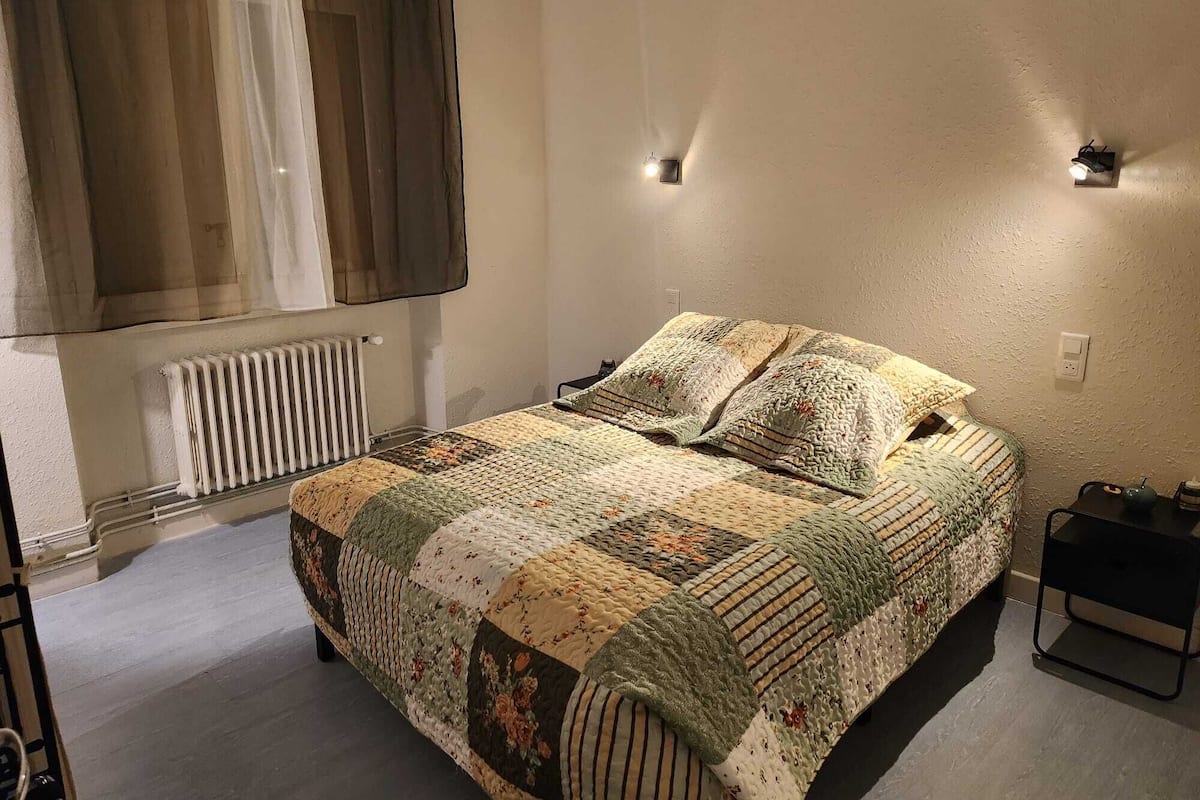 A bedroom with a large bed, a radiator, a window with curtains, and two wall-mounted lights.