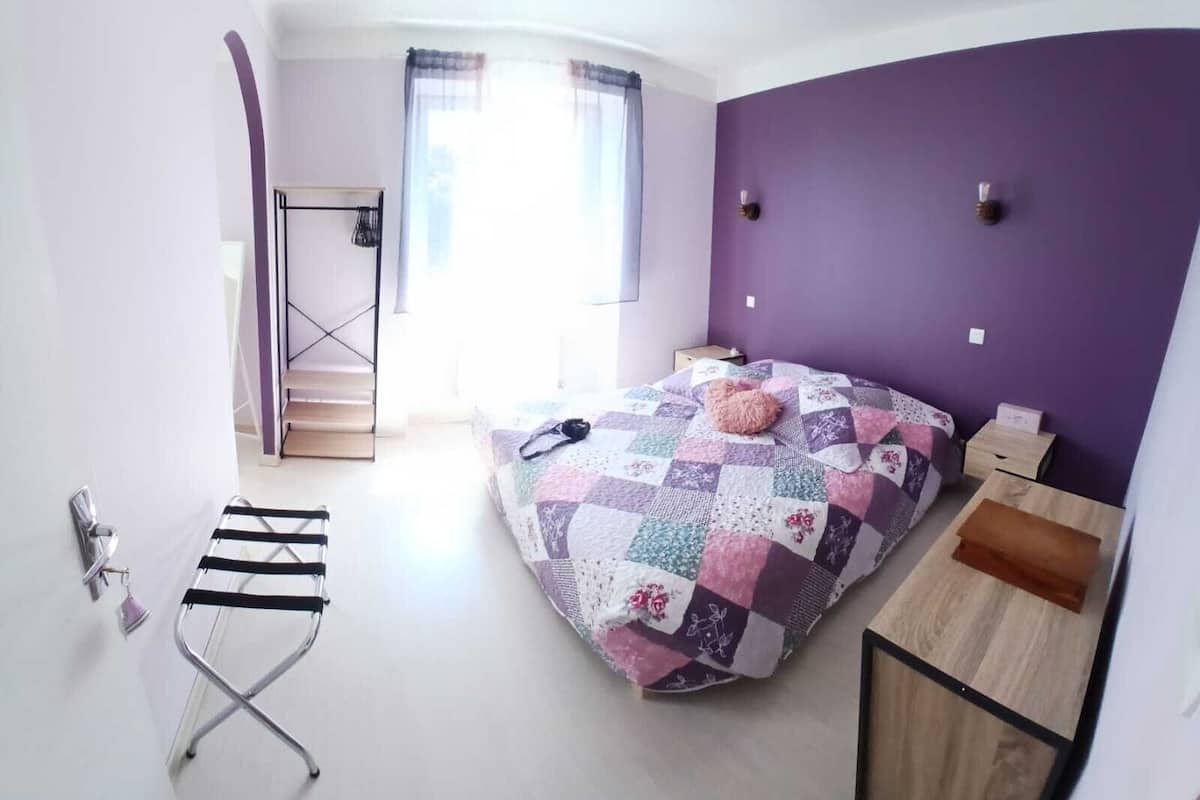 A bedroom with a bed, a desk, a chair, and a window with curtains.
