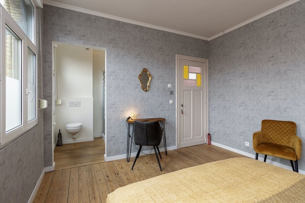Een kamer met een bed, een bureau met stoel, een deur en een raam.