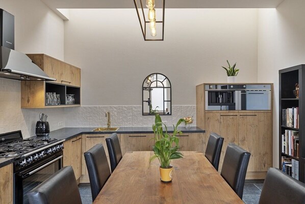 A modern kitchen with a wooden dining table, chairs, a stove, and a built-in oven.