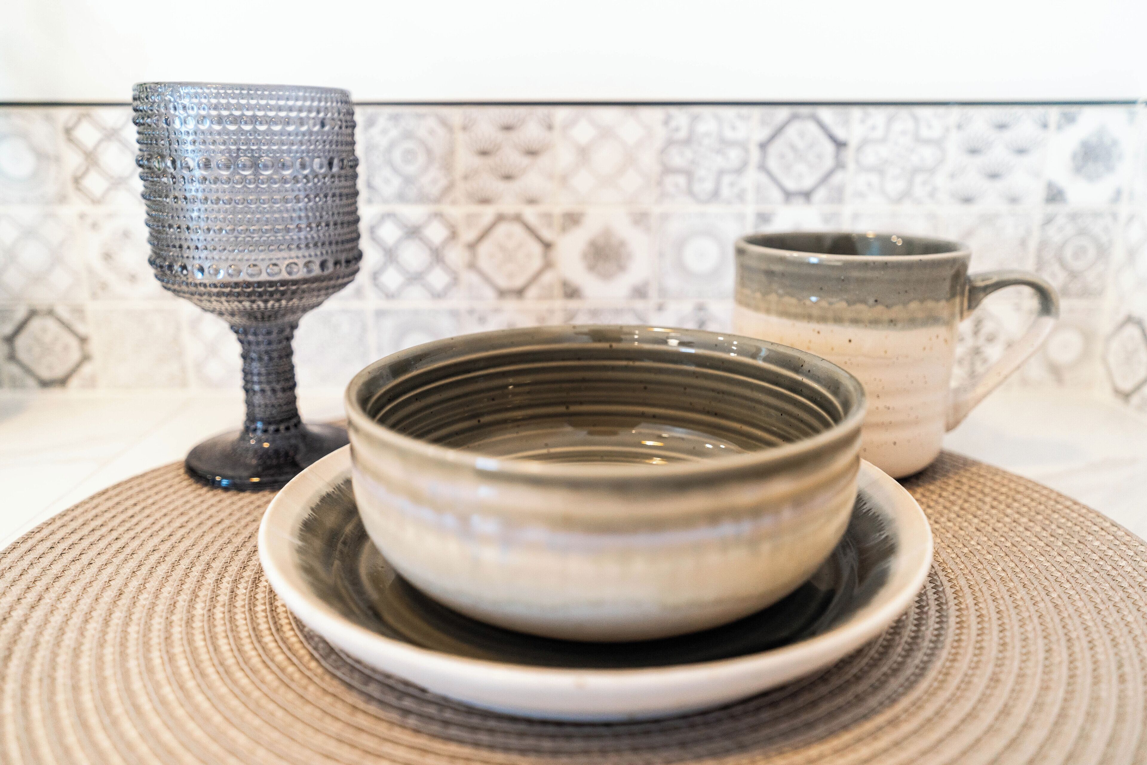 A ceramic bowl on a plate, a ceramic mug, and a textured glass on a woven placemat.