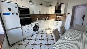 A modern kitchen with white cabinets, a built-in oven, a washing machine, and a dining area with a patterned table. - Charming 2-bed Apartment in Baku City Center (Baku)