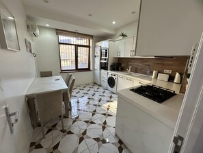A compact kitchen with a washing machine, a gas stove, and a dining area with a table and chairs. - Charming 2-bed Apartment in Baku City Center (Baku)