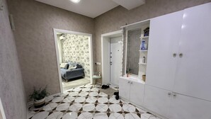 A room with a patterned floor, a grey sofa, a white wardrobe, and a bathroom with a shower and a mirror. - Charming 2-bed Apartment in Baku City Center (Baku)